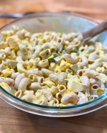 macaroni salad in a glass bowl with a wooden spoon on a wooden surface