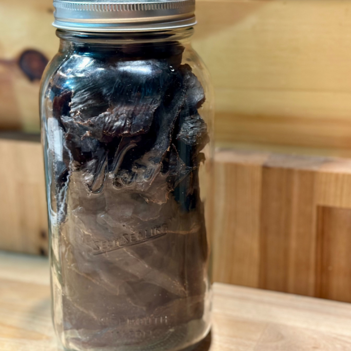 deer jerky in a half gallon mason jar on a wooden counter