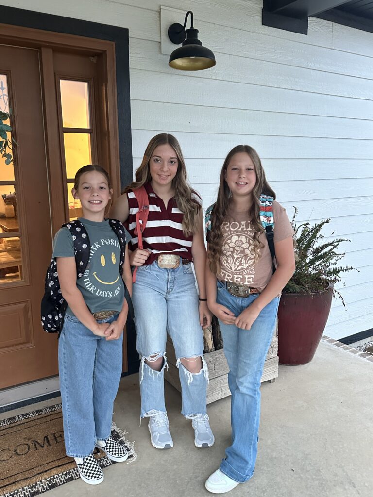 3 girls standing on a porch with backpacks on