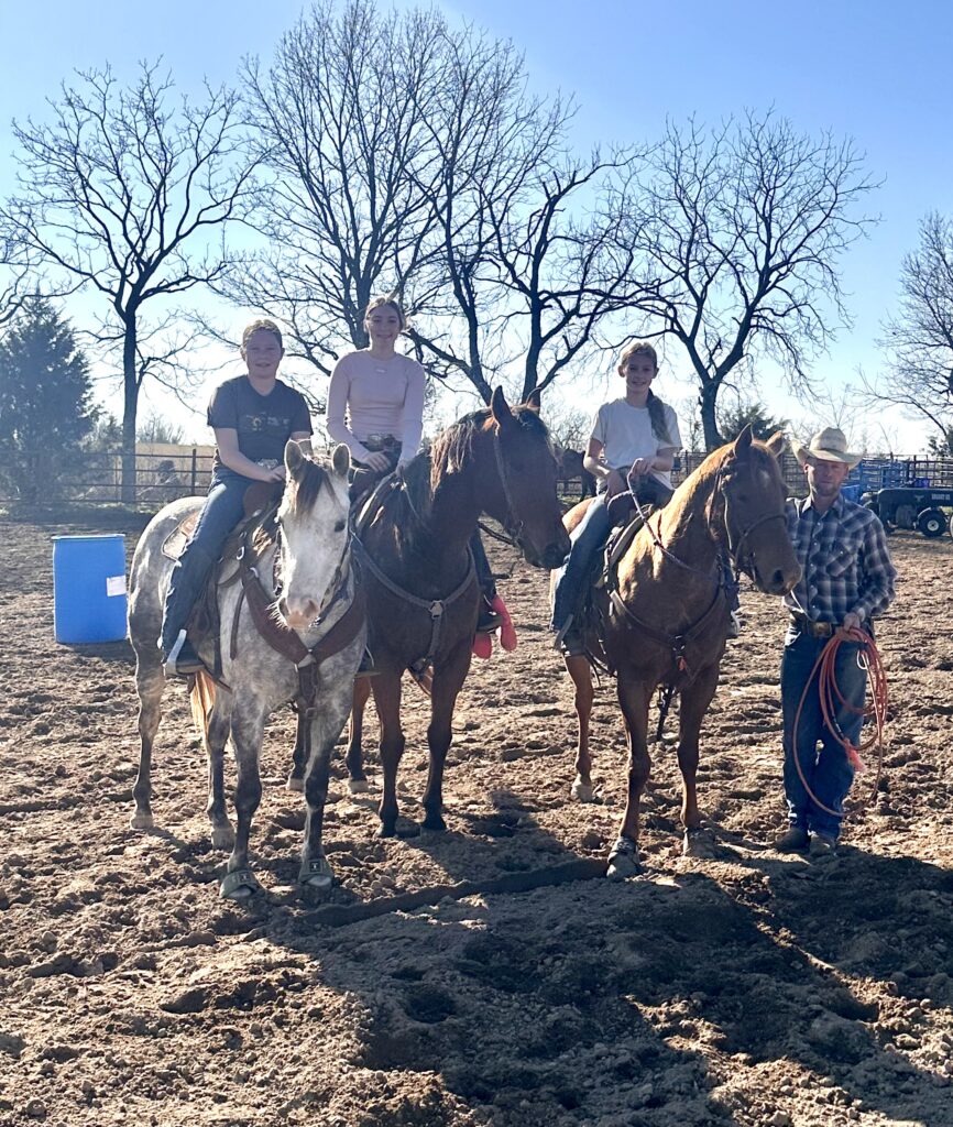 3 girls on horses with a man standing next to them holding a rope