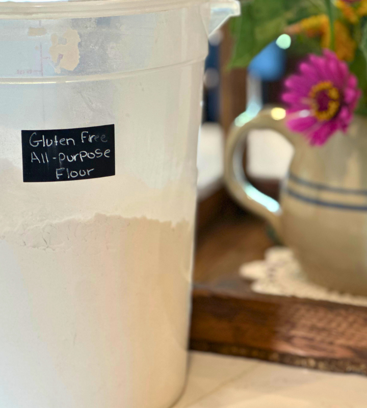 plastic bucket with flour label all purpose flour, and a pitcher with fresh flower