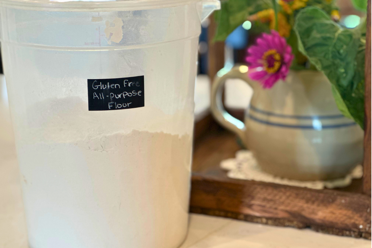 plastic bucket with flour label all purpose flour, and a pitcher with fresh flower